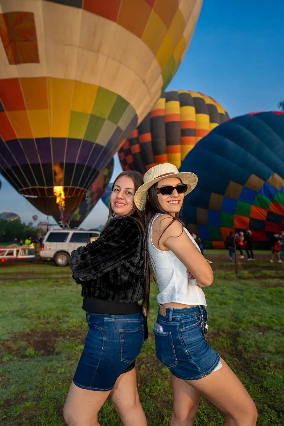 Two friends pose back to back as the burner fires up a hot air balloon in Teotihuacan at dawn