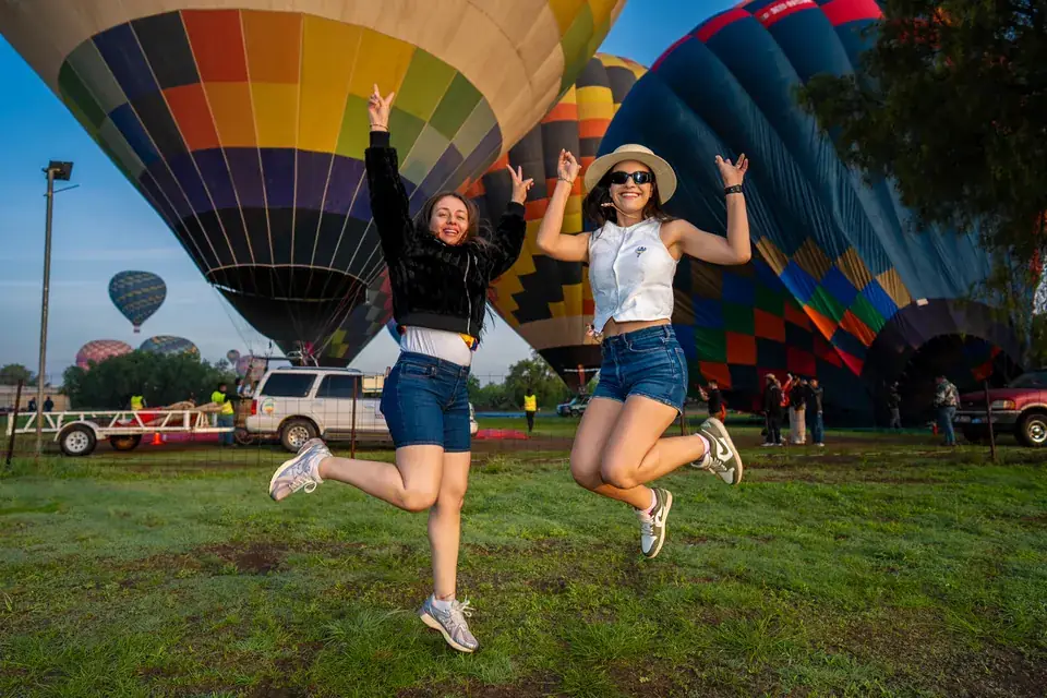 Dos amigas saltan de alegría sobre el pasto frente a los globos ya inflados en Teotihuacán