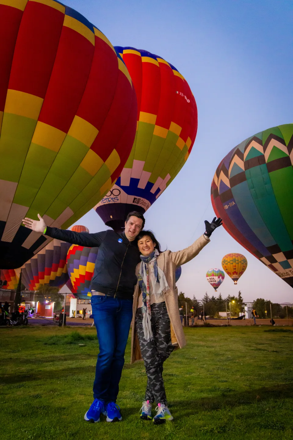 Pareja con los brazos extendidos ante vibrantes globos en la hora azul sobre Teotihuacán