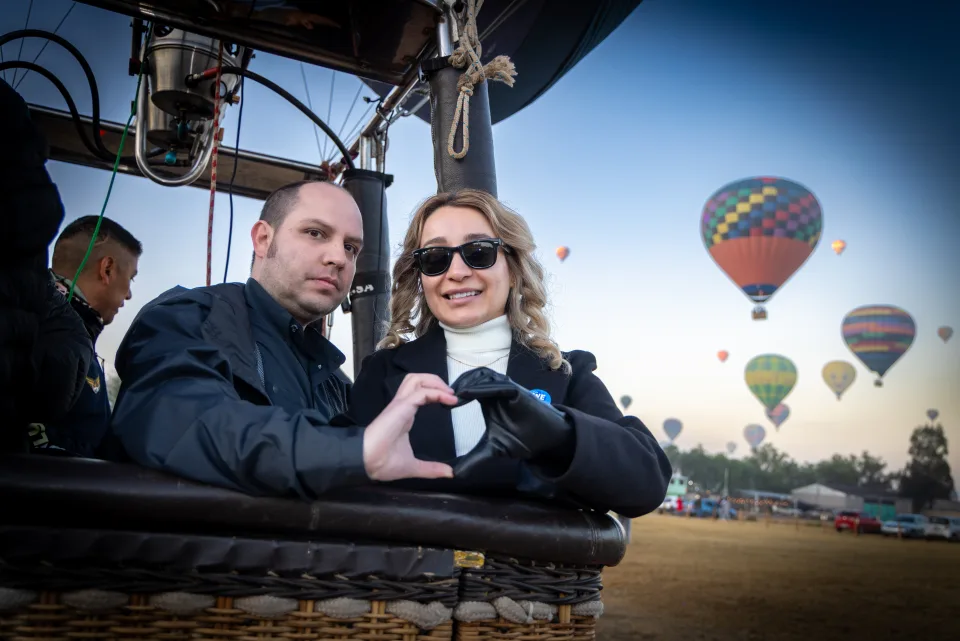 Pareja formando un corazón con las manos dentro de la canastilla al amanecer