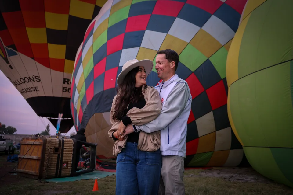 Pareja mirándose junto a coloridos globos inflándose al amanecer
