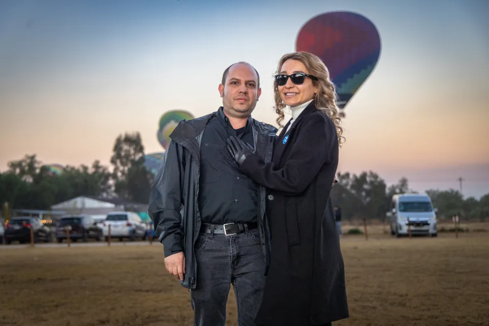 Pareja posando junta con globos y el cielo del amanecer detrás
