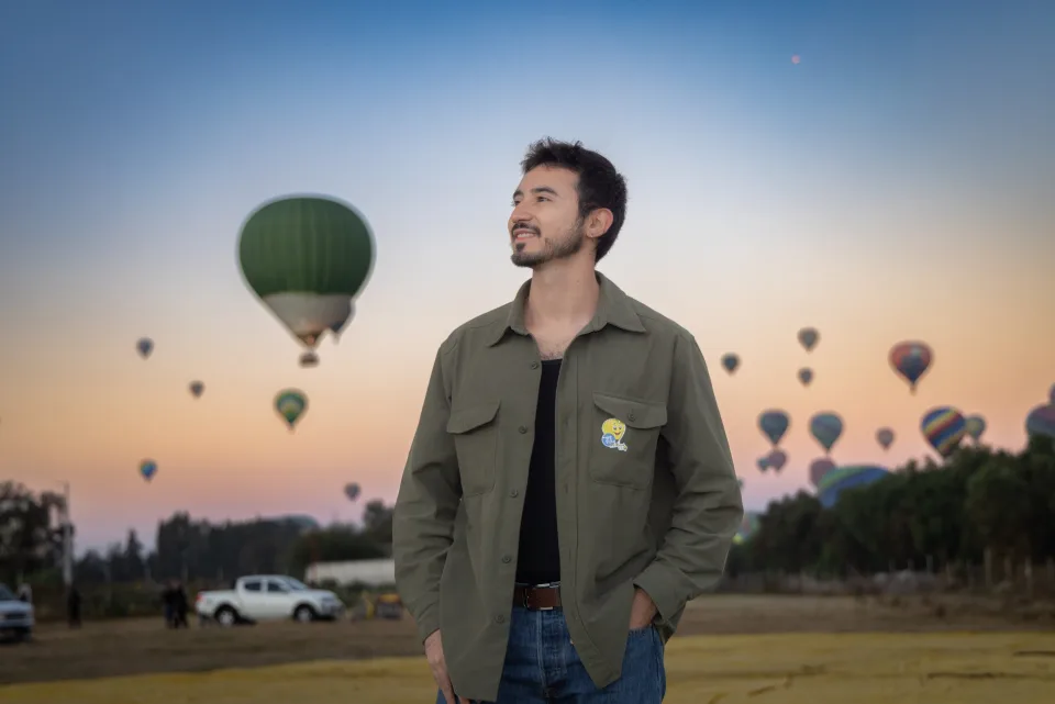 Viajero en el campo de despegue mientras decenas de globos cruzan el amanecer de Teotihuacán
