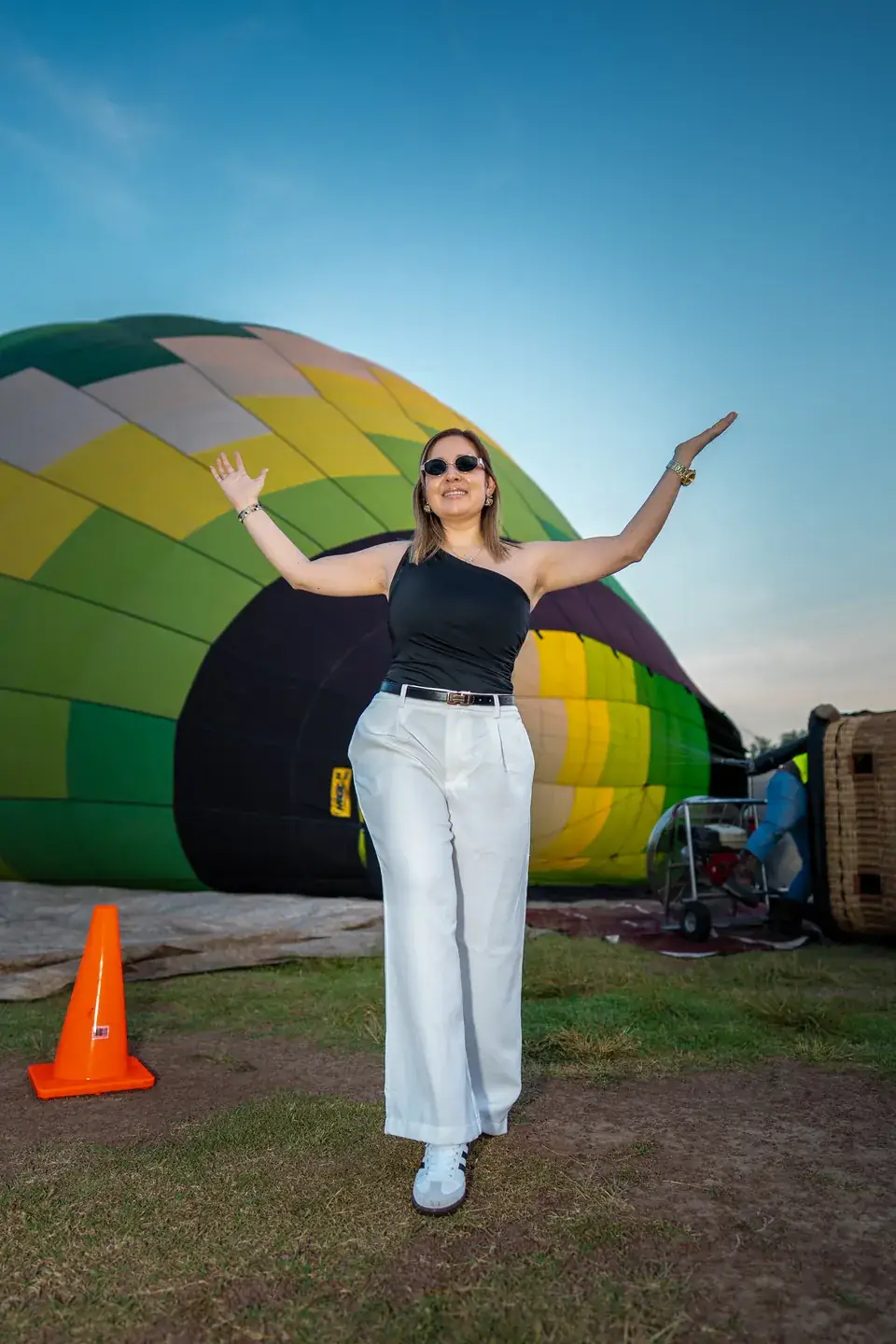 Smiling woman opens her arms beside an inflated green hot air balloon under Teotihuacan's blue sky