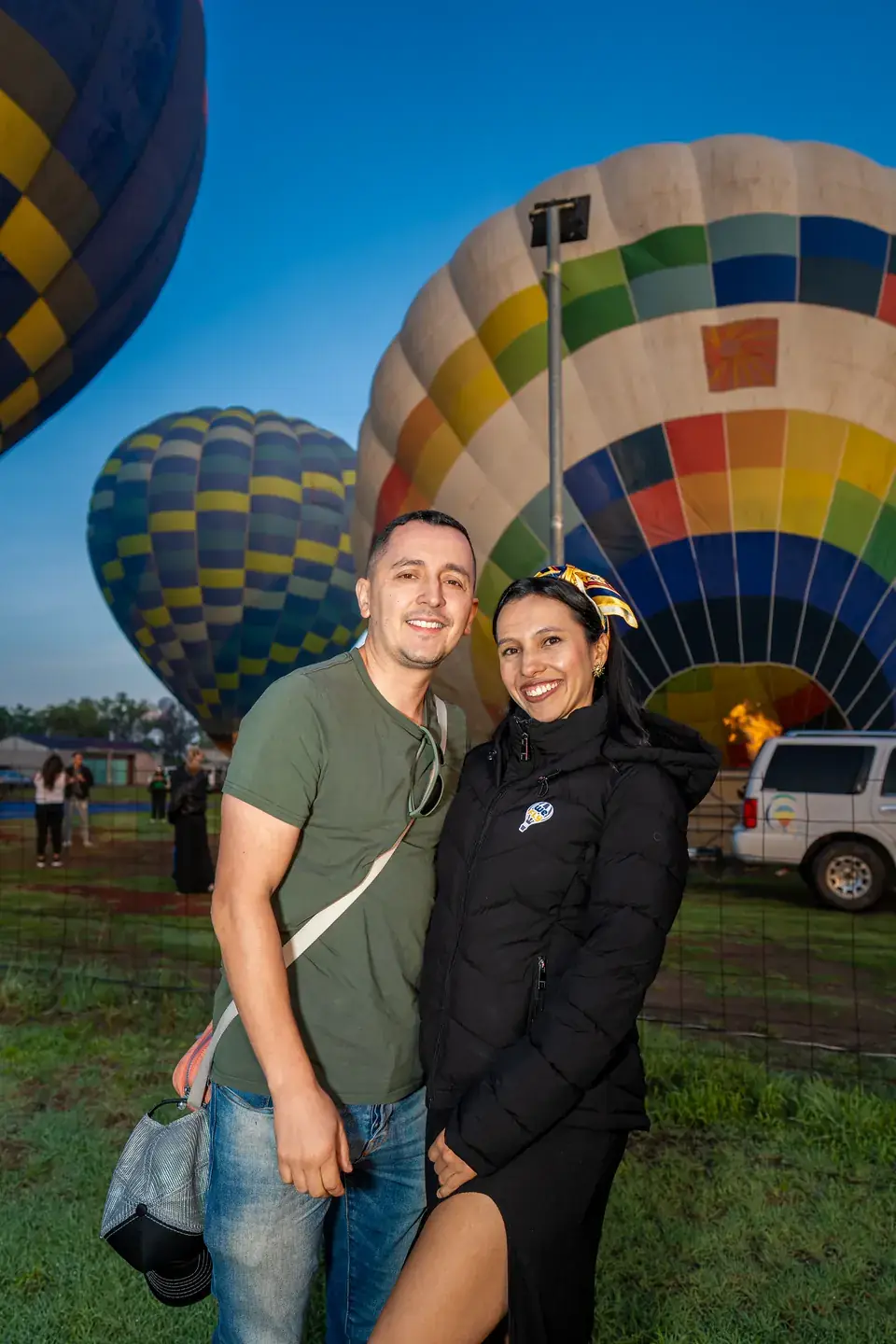 Couple hugging and smiling in front of a hot air balloon inflating with burner flame