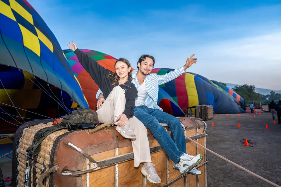Couple sitting on a balloon basket with arms outstretched, celebrating at dawn in Teotihuacan
