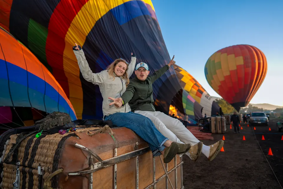 Couple cheering while sitting on a hot air balloon basket as the envelope inflates