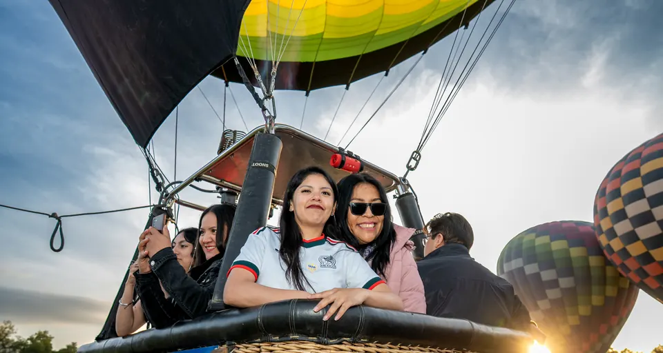 Four passengers leaning out of the balloon basket as the sun rises behind them in Teotihuacan