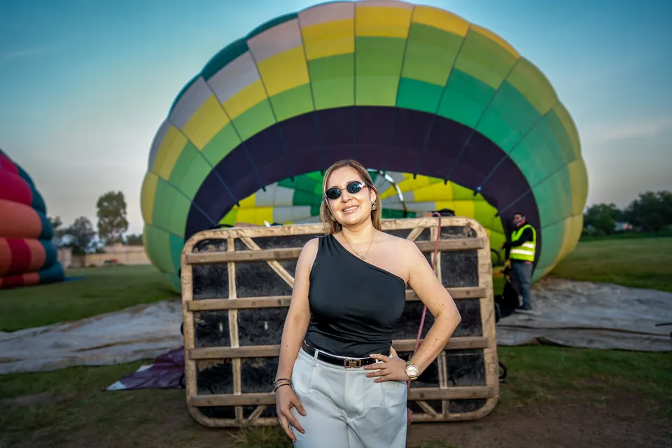 Pasajera sonriendo junto a la canasta y al globo verde inflándose al amanecer en Teotihuacán