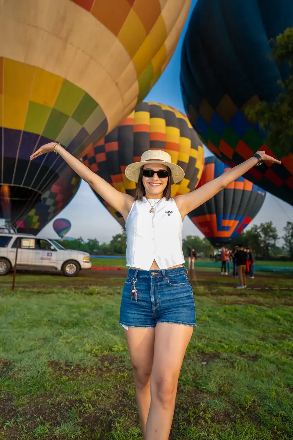 Traveler in a straw hat opens her arms before three inflated hot air balloons at sunrise in Teotihuacan