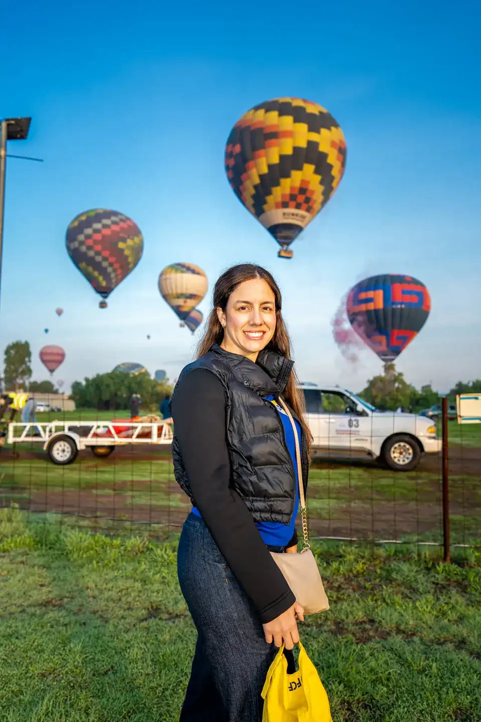 Smiling woman at the launch field as several hot air balloons rise at sunrise over Teotihuacan