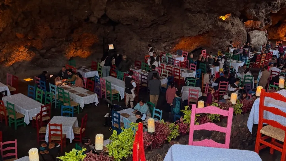 The dining room of La Gruta restaurant in Teotihuacan, with laid tables and brightly painted handmade chairs